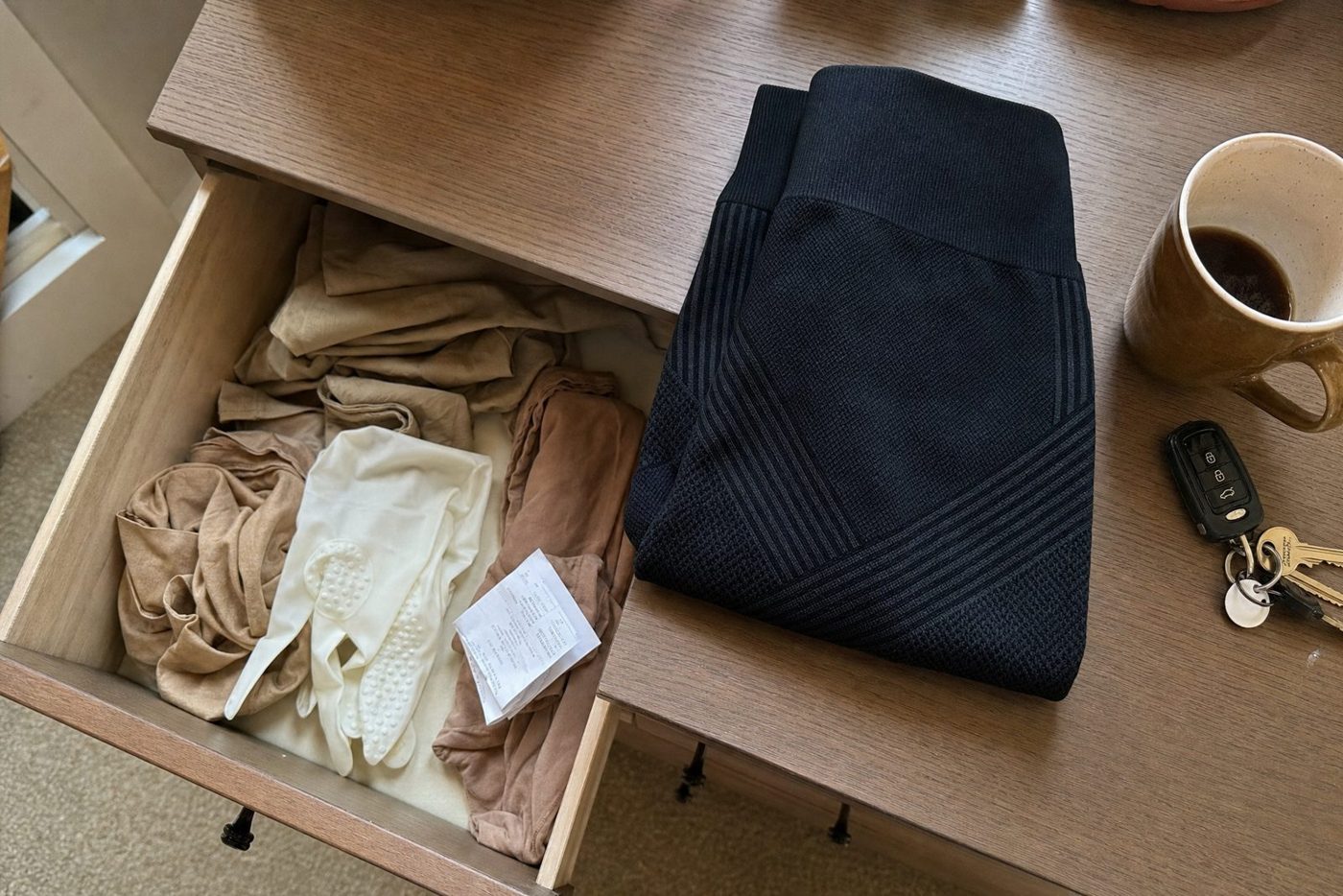 Otevřený šuplík komody plný nenošených béžových zdravotních punčoch, na nich leží složené černé kompresní legíny